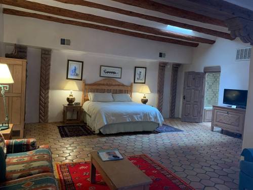 Spacious bedroom with wooden beams, a king bed, cozy seating, and a TV, featuring warm, earthy tones and tile flooring.