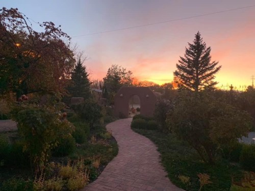 A winding brick path leads through lush greenery towards a sunset sky with vibrant colors.