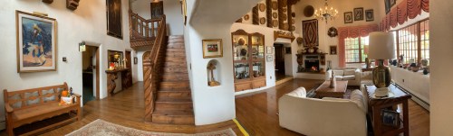 A spacious living room with wooden accents, a staircase, and a cozy seating area, adorned with artwork and decor.
