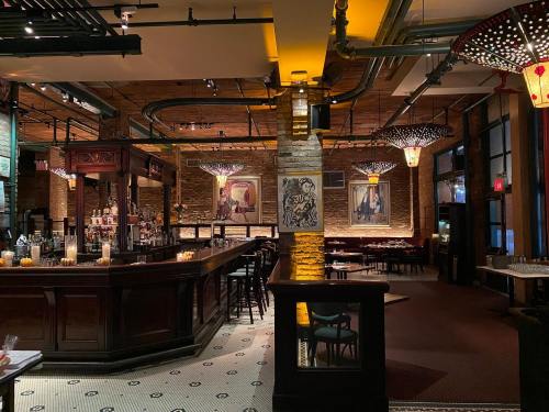 A stylish restaurant interior featuring a wooden bar, elegant lighting, and artistic decor on the walls.