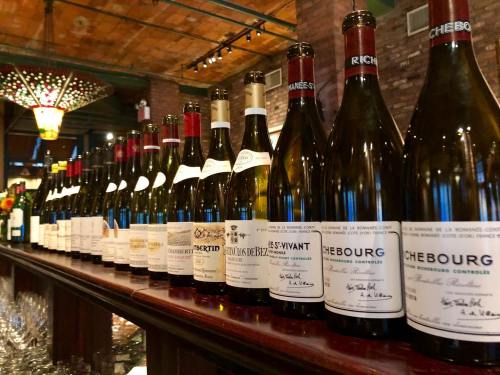 A row of wine bottles with elegant labels displayed on a wooden bar in a cozy, dimly lit setting.