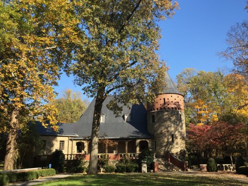 A stone castle with a turret surrounded by colorful autumn trees and a clear blue sky.
