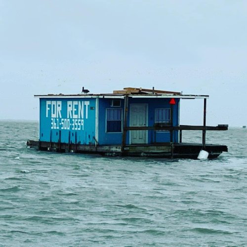 A floating house for rent on water, painted blue with a sign displaying the rental phone number.