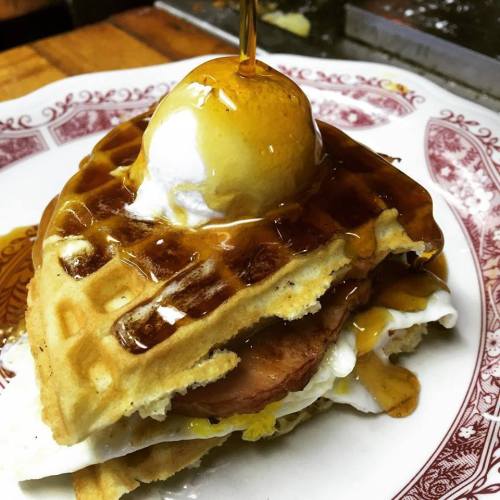 A delicious waffle topped with a fried egg, bacon, and drizzled with syrup, served on a decorative plate.