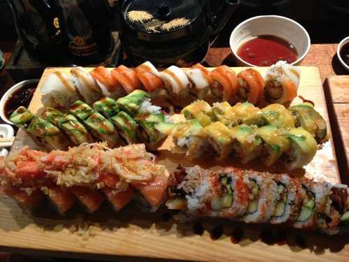 A wooden platter featuring various sushi rolls, including salmon, avocado, and crab, with dipping sauces in the background.