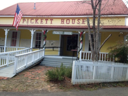 A yellow building with "Pickett House" sign, American flag, and festive decorations, surrounded by a white picket fence.