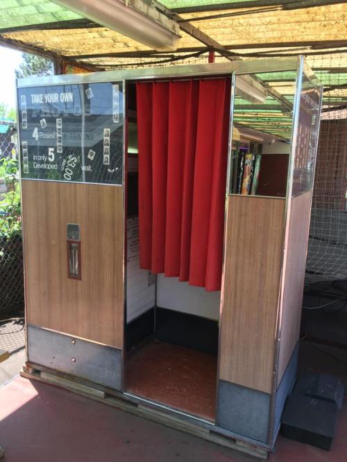 A vintage photo booth with red curtains and a wooden exterior, labeled "Take Your Own" for instant photo development.