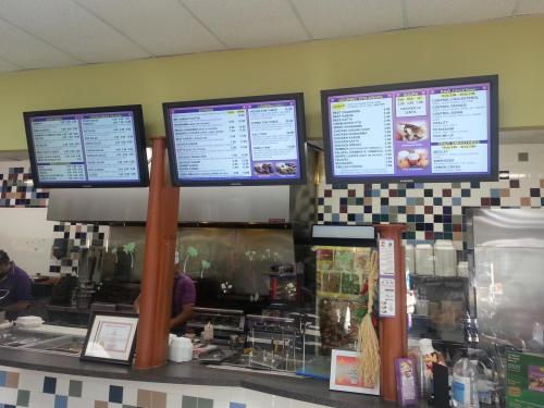 Menu boards displaying food options and prices in a casual dining restaurant with a kitchen in the background.
