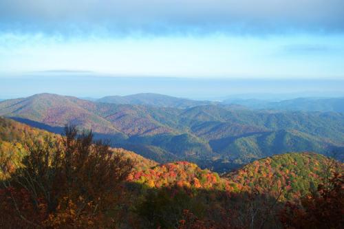 A panoramic view of colorful autumn mountains, with vibrant foliage and a clear sky in the background.