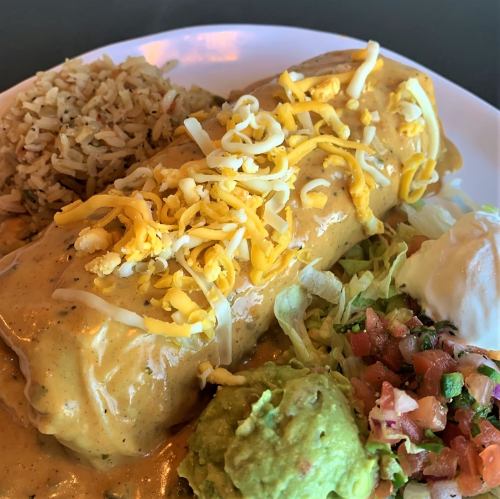 A plate featuring a large burrito topped with cheese, served with rice, guacamole, lettuce, and pico de gallo.