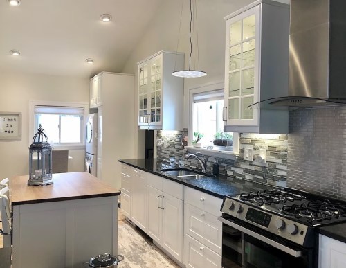 Modern kitchen with white cabinets, a wooden island, stainless steel appliances, and a stylish backsplash. Bright and airy space.