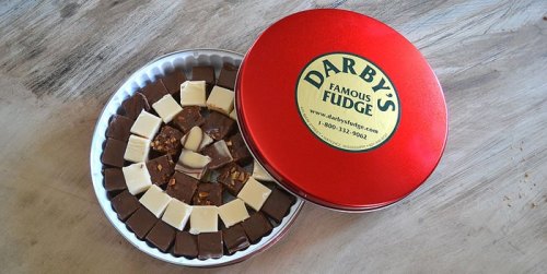 A red tin filled with assorted fudge pieces, including chocolate and white fudge, arranged in a circular pattern.