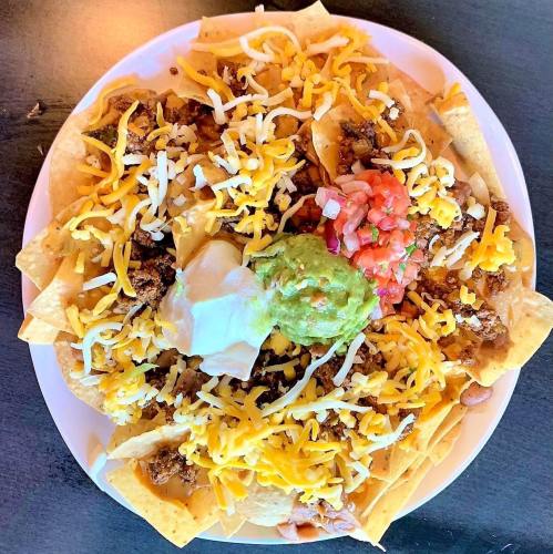 A plate of nachos topped with cheese, ground beef, guacamole, salsa, and sour cream on a bed of tortilla chips.