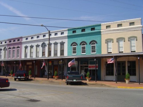 Historic storefronts in a small town, featuring colorful facades and American flags along the sidewalk.