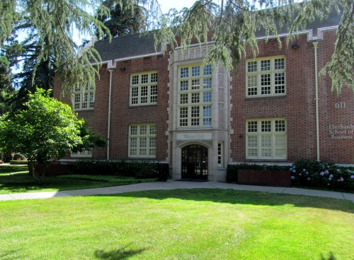 Brick building with large windows, surrounded by green grass and trees, labeled as the DeBartolo School of Business.
