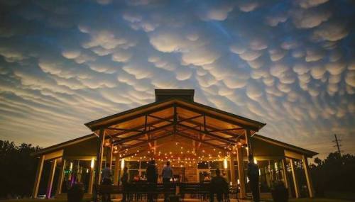 A modern building with string lights under a dramatic sky filled with unique cloud formations at dusk.