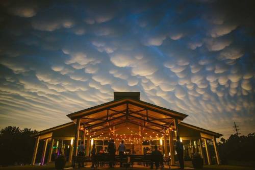 A gathering under a dramatic sky with mammatus clouds, illuminated by string lights at a cozy outdoor venue.