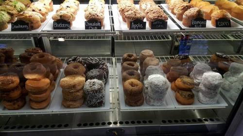 A display case filled with various donuts and muffins, including chocolate, apple, and blueberry flavors.