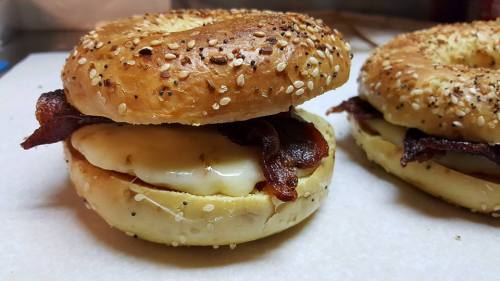 A toasted sesame bagel sandwich with bacon and melted cheese, resting on a white surface.