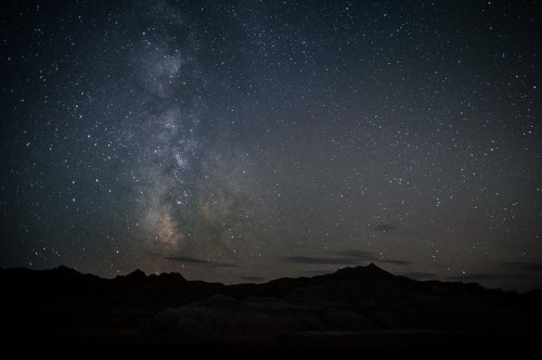 A starry night sky filled with the Milky Way over dark, rugged terrain.