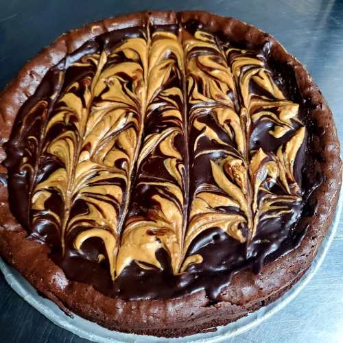 A rich chocolate cake with a glossy peanut butter swirl design on top, set on a silver surface.