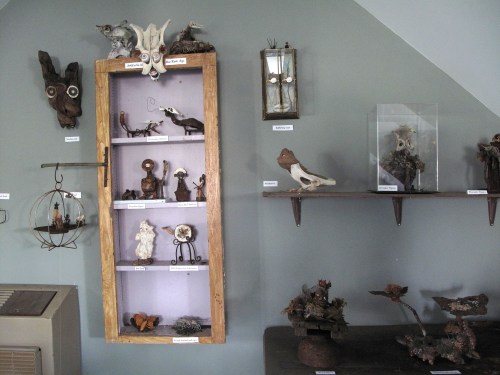 A display of various artistic sculptures and curiosities on shelves and walls, featuring natural materials and unique designs.