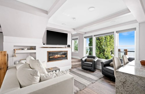 Modern living room with a cozy sofa, two chairs, a fireplace, and large windows overlooking a scenic view.