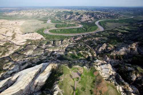 Aerial view of winding river through rugged terrain and green valleys, showcasing layered rock formations and natural beauty.