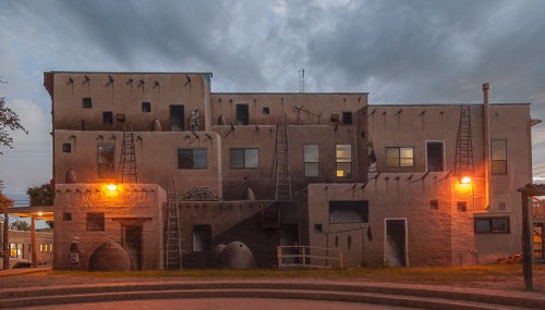 A large, mural-covered building with ladders and warm lighting, set against a cloudy evening sky.