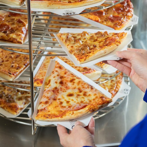 A person takes a slice of pizza from a display rack filled with various pizza slices.