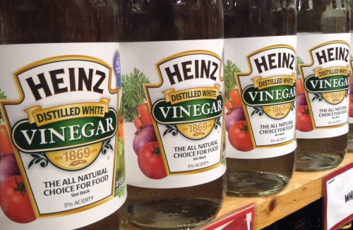 Four bottles of Heinz Distilled White Vinegar lined up on a shelf, featuring a label with tomatoes and the year 1869.