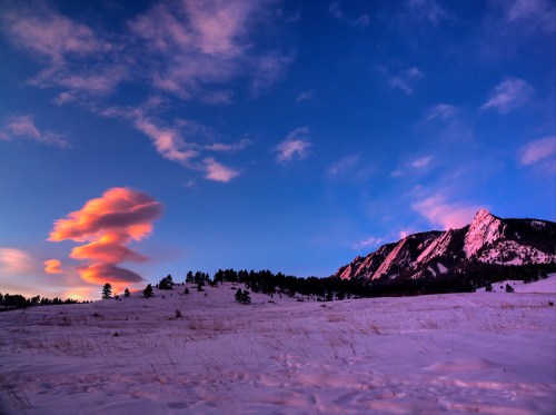 A vibrant sunset sky with pink clouds above snow-covered mountains and a grassy foreground.