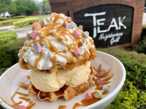 A delicious dessert featuring a waffle topped with ice cream, whipped cream, caramel drizzle, and colorful marshmallows.