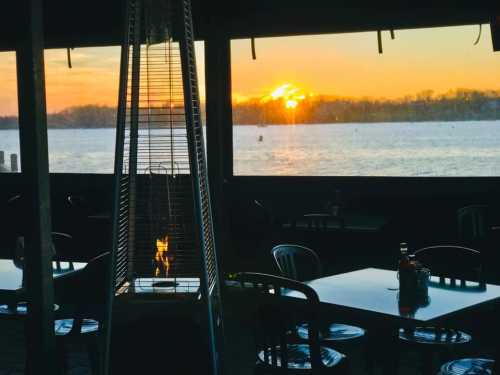 A cozy restaurant setting with a heater, overlooking a sunset by the water.