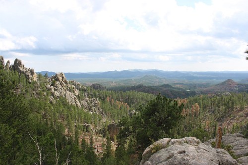 A panoramic view of lush green mountains and rocky formations under a cloudy sky.