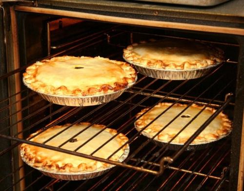 Four golden-brown pies baking in an oven, resting on wire racks.