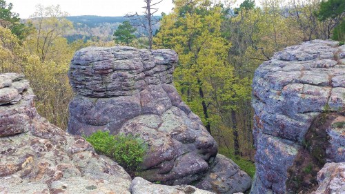 Two large rock formations resembling faces, surrounded by trees and greenery in a natural landscape.
