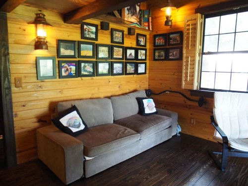 Cozy wooden room featuring a sofa, framed photos on the wall, and warm lighting from lamps.