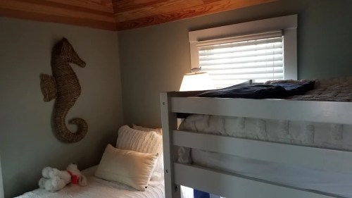 A cozy bedroom featuring a bunk bed, a stuffed animal, and a seahorse wall decoration. Natural light from a window.