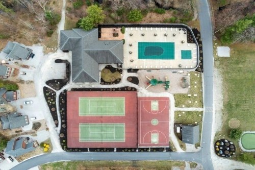 Aerial view of a property featuring a house, tennis courts, basketball courts, and a pool area surrounded by landscaping.