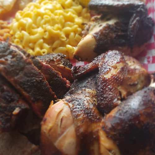 Close-up of smoked chicken pieces with a side of creamy macaroni and cheese on a red-checkered plate.