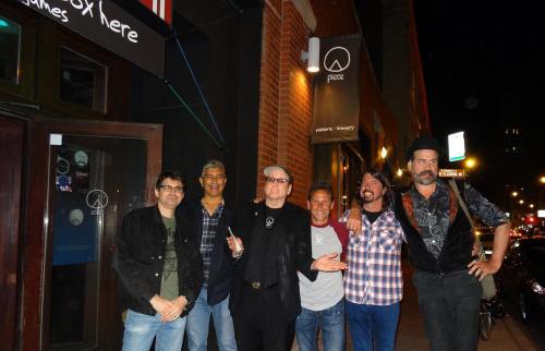 A group of six men stands outside a restaurant at night, smiling and posing for the camera.