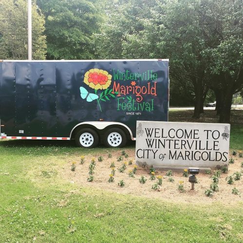 Sign welcoming visitors to Winterville, home of the Marigold Festival, with a colorful trailer in the background.