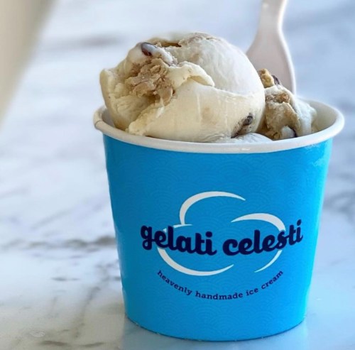 A blue cup of gelato with chunks of cookie dough and vanilla ice cream, sitting on a marble surface.