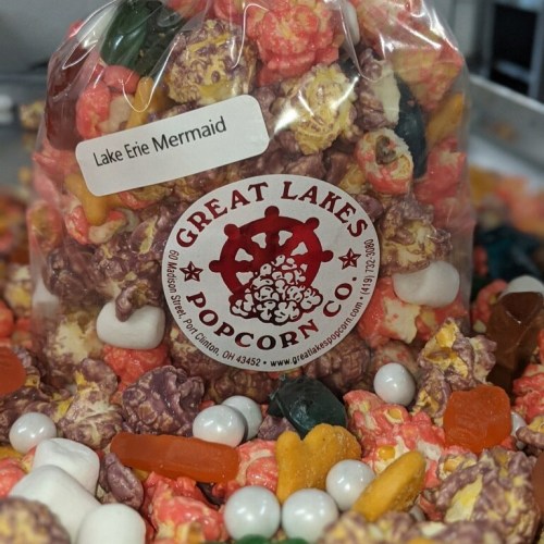 A bag of colorful popcorn labeled "Lake Erie Mermaid" surrounded by various candies and snacks.