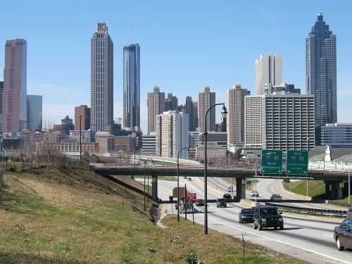 City skyline of Atlanta with tall buildings, a highway in the foreground, and clear blue skies.