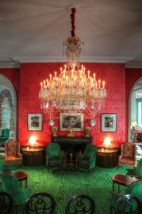 A luxurious room with a large chandelier, red walls, green carpet, and elegant furniture, creating an opulent atmosphere.
