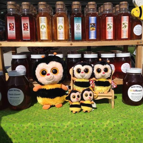 A display of honey jars and cute bee plush toys on a green tablecloth at a market.