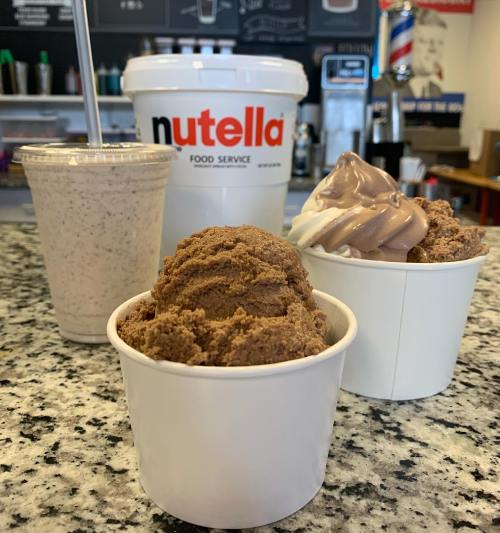 Two cups of chocolate ice cream, one with swirled vanilla, a milkshake, and a large Nutella bucket on a counter.