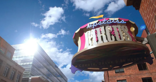 Colorful circus sign against a bright blue sky with clouds, promoting a venue for creativity and fun.